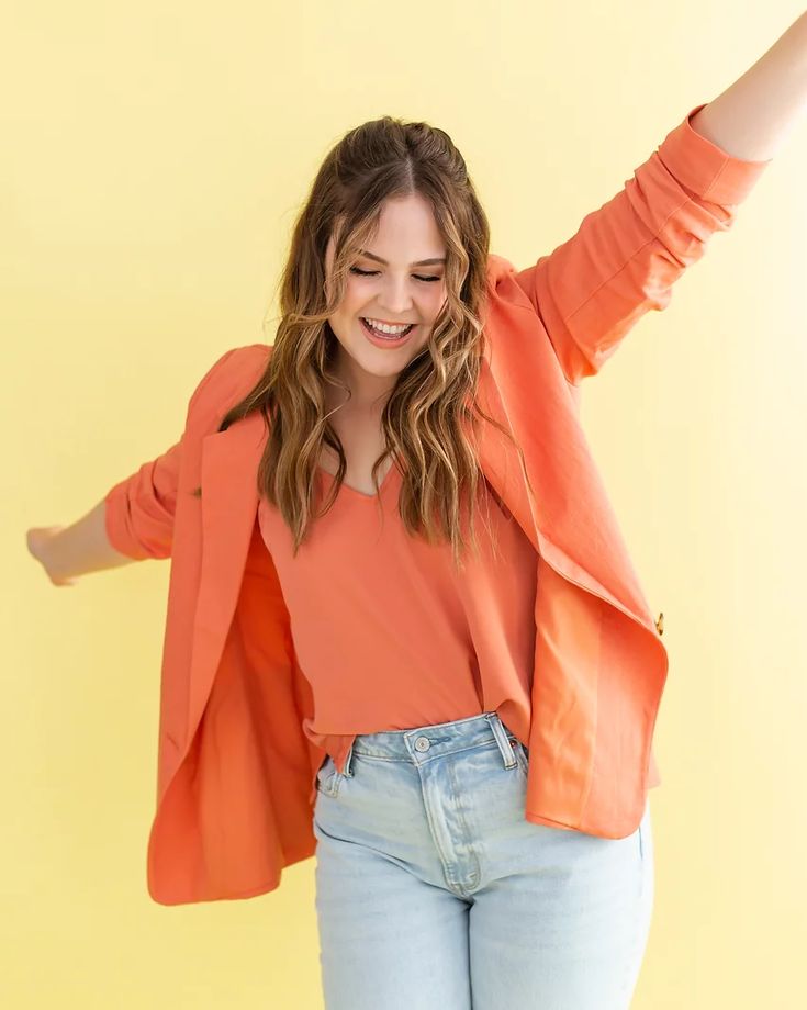 a woman in an orange shirt and jeans is holding her arms out to the side