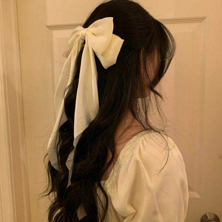 a woman with long hair wearing a white shirt and a bow in her hair is looking at the door