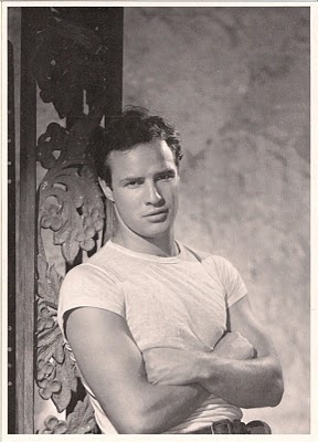 black and white photograph of a young man leaning against a wall with his arms crossed