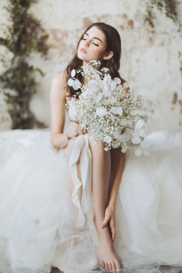 a woman in a wedding dress holding a bouquet of flowers and posing for the camera