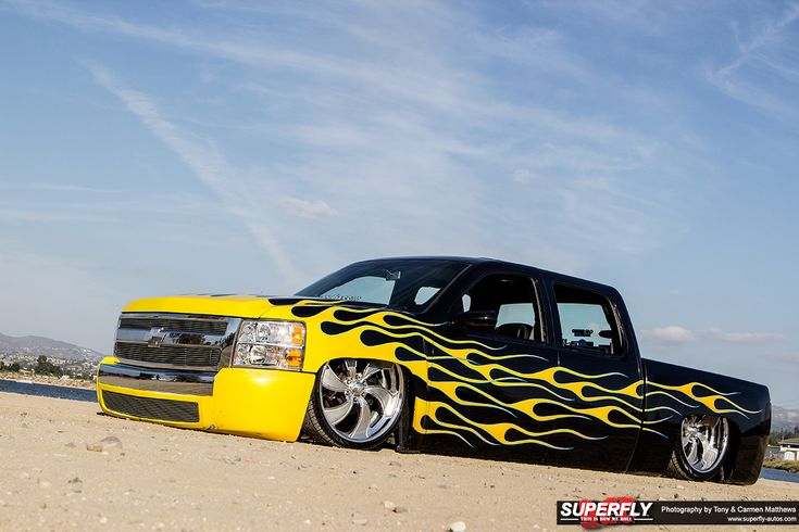 a black and yellow truck with flames painted on it's hood sitting in the sand