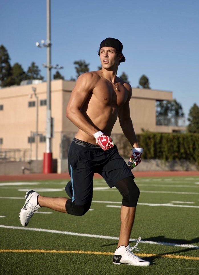 a shirtless man running on a football field with his gloved hand in the air