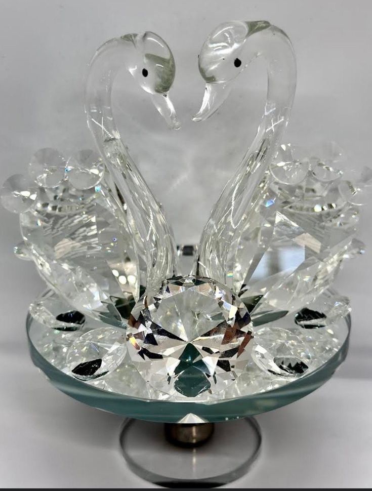 a glass swan sculpture on top of a crystal bowl with two birds in the middle