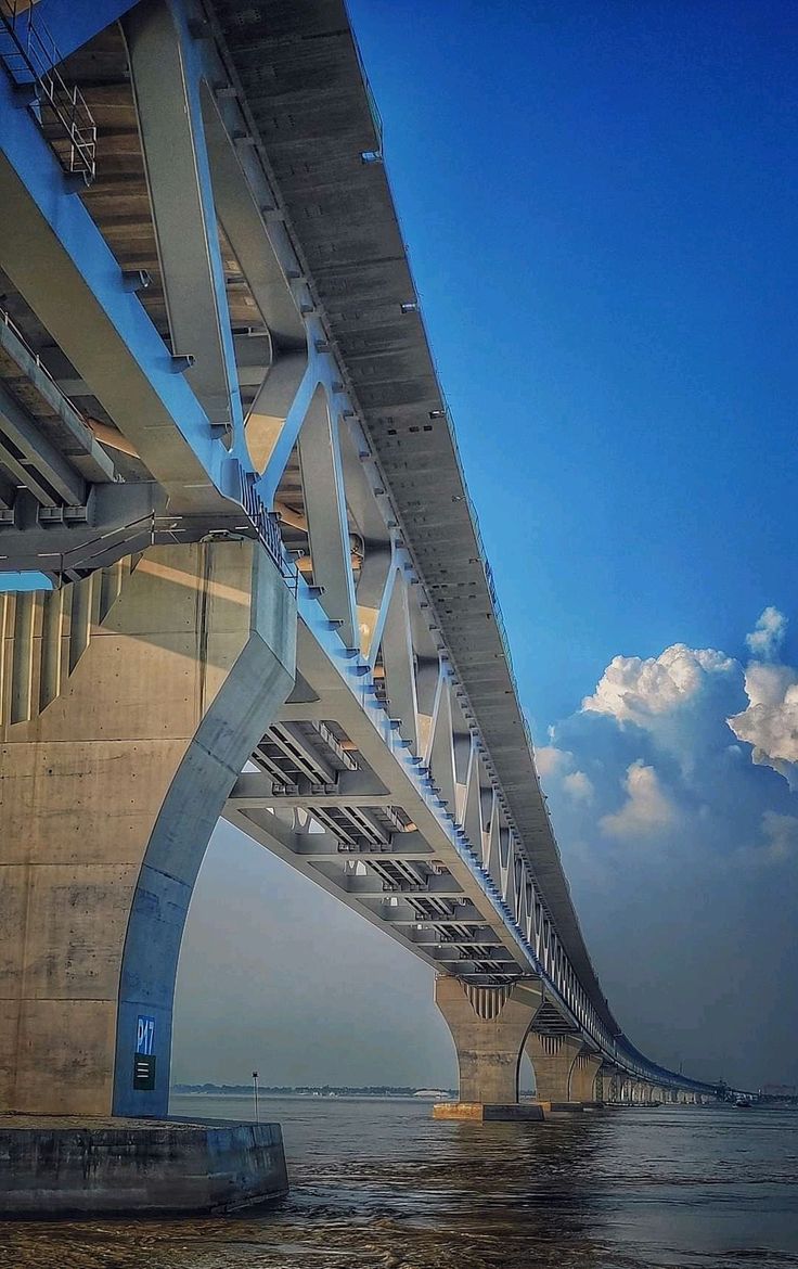 the underside of a bridge over water with clouds in the sky and blue skies above