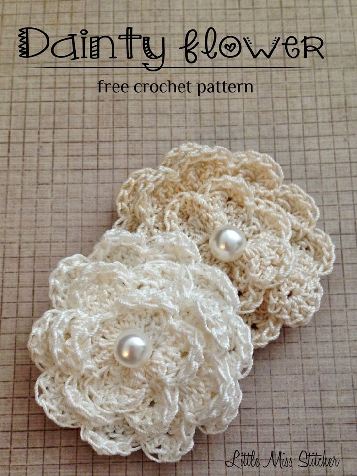 two crochet flower broochies with pearls on them sitting on a piece of cloth