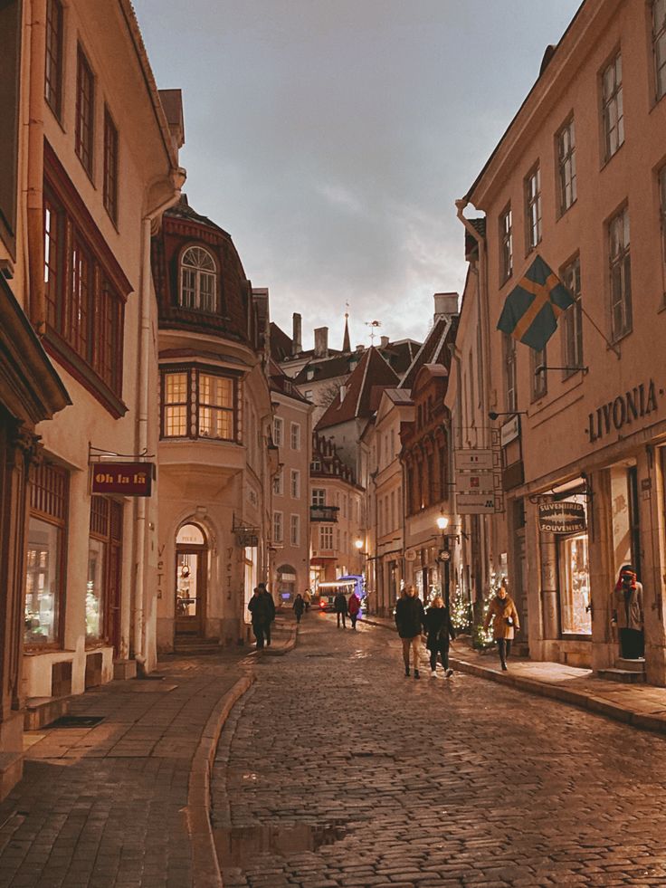 people are walking down the cobblestone street in an old european town at dusk