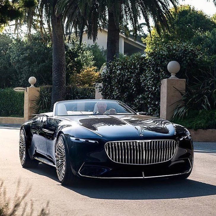 a black car parked on the side of a road next to some trees and bushes