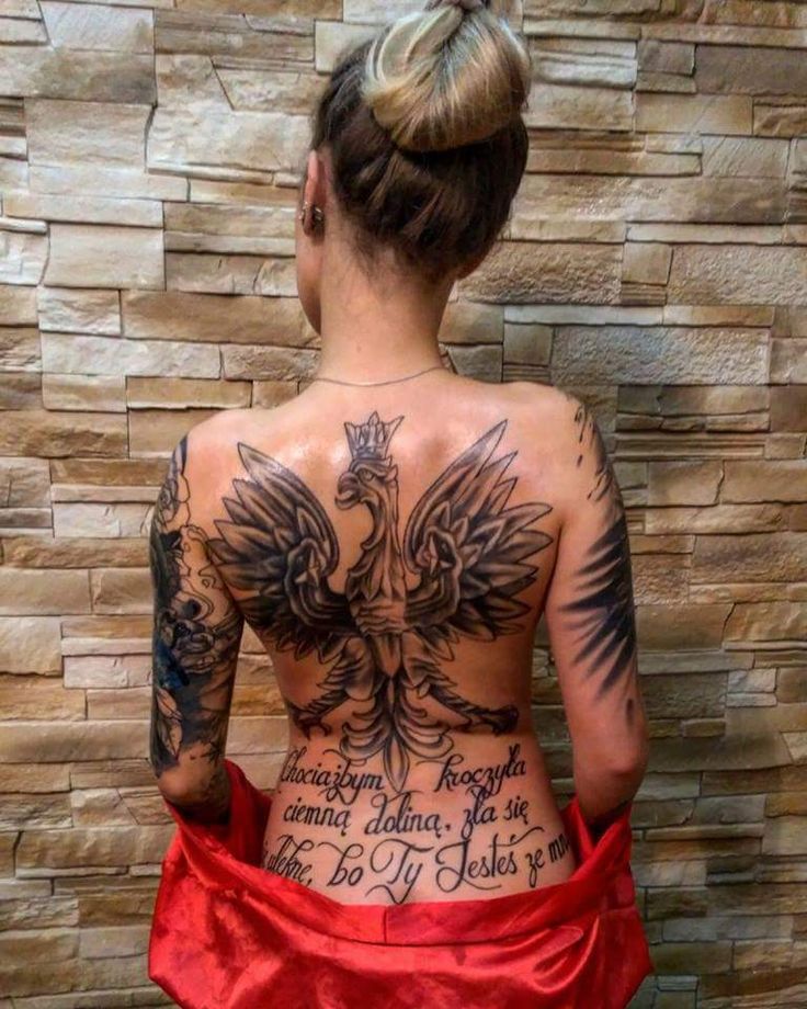 a woman with tattoos on her back is standing in front of a stone wall and wearing a red skirt