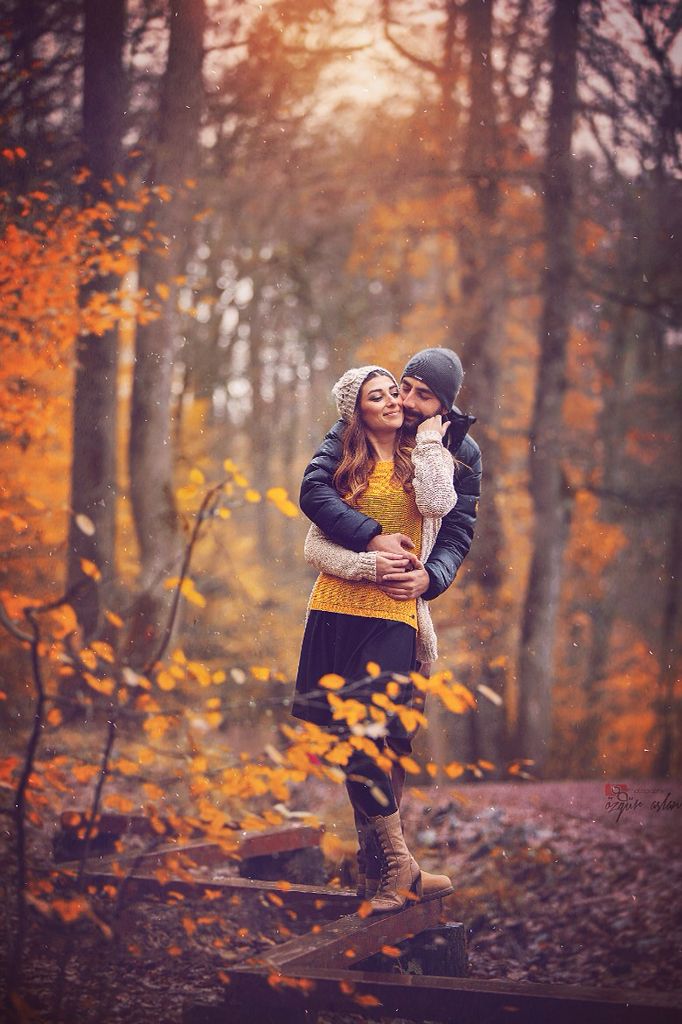 a man and woman hugging in the woods with autumn leaves on the ground behind them