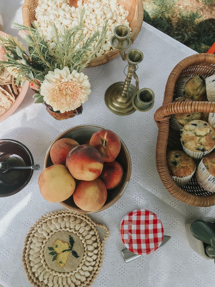 a table topped with baskets filled with peaches and muffins on top of a white table cloth