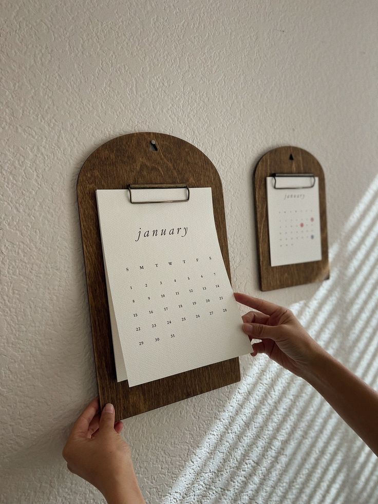 a person holding up a calendar on a wall with two magnets attached to it