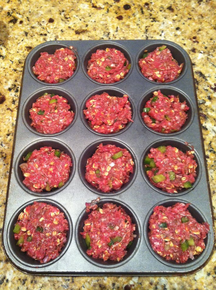 a muffin tin filled with lots of red meat and green peppers sitting on top of a marble counter