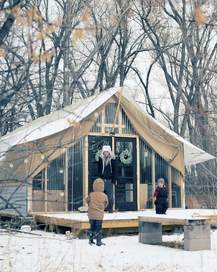 two people are standing outside in the snow near a small building with a door and windows