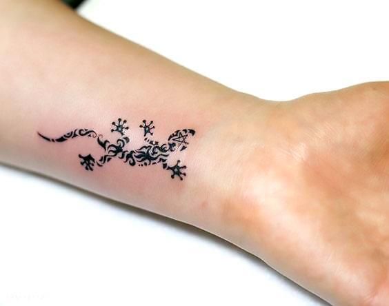 a small black lizard tattoo on the left inner arm and wrist, with flowers all over it