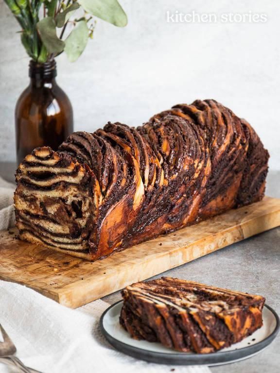 a loaf of chocolate marbled bread on a wooden cutting board next to a vase with flowers