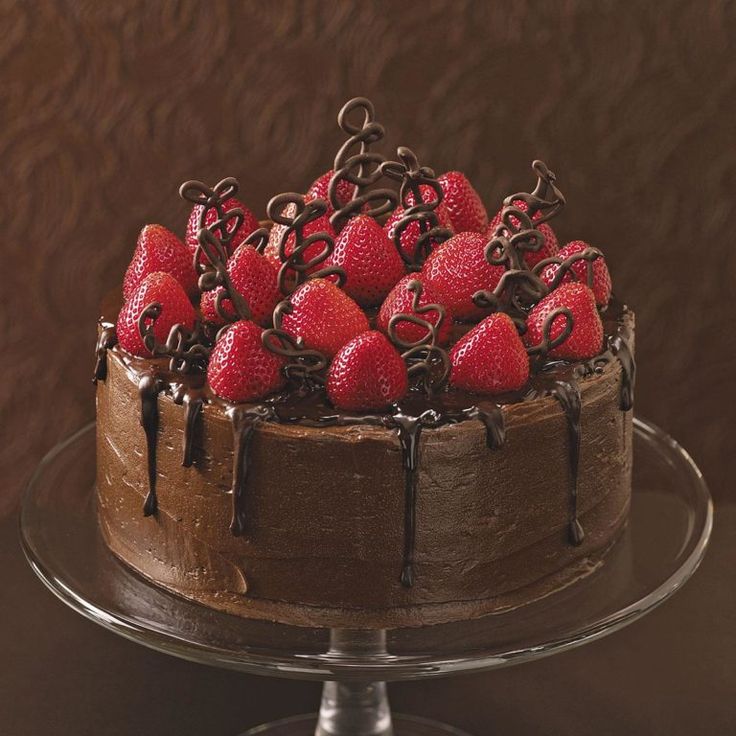 a chocolate cake topped with strawberries on top of a glass plate next to a brown wall