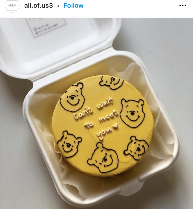 a yellow cake in a plastic container with winnie the pooh decorations on it's side