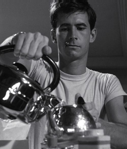 black and white photograph of a man pouring water into a teapot on a table