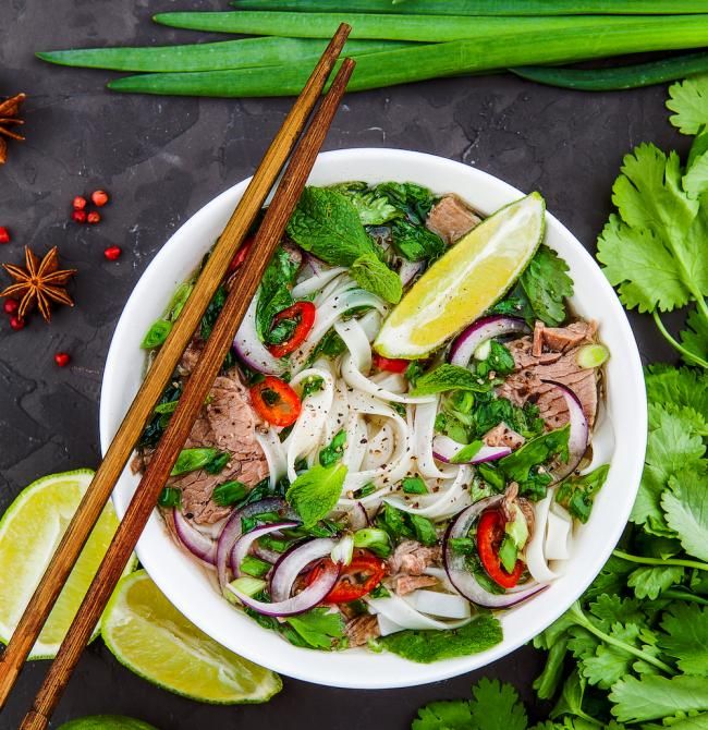 a white bowl filled with meat and vegetables next to chopsticks on a table