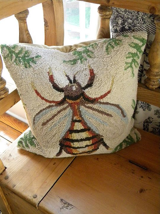 a decorative pillow with a bee on it sitting on a wooden chair next to a window