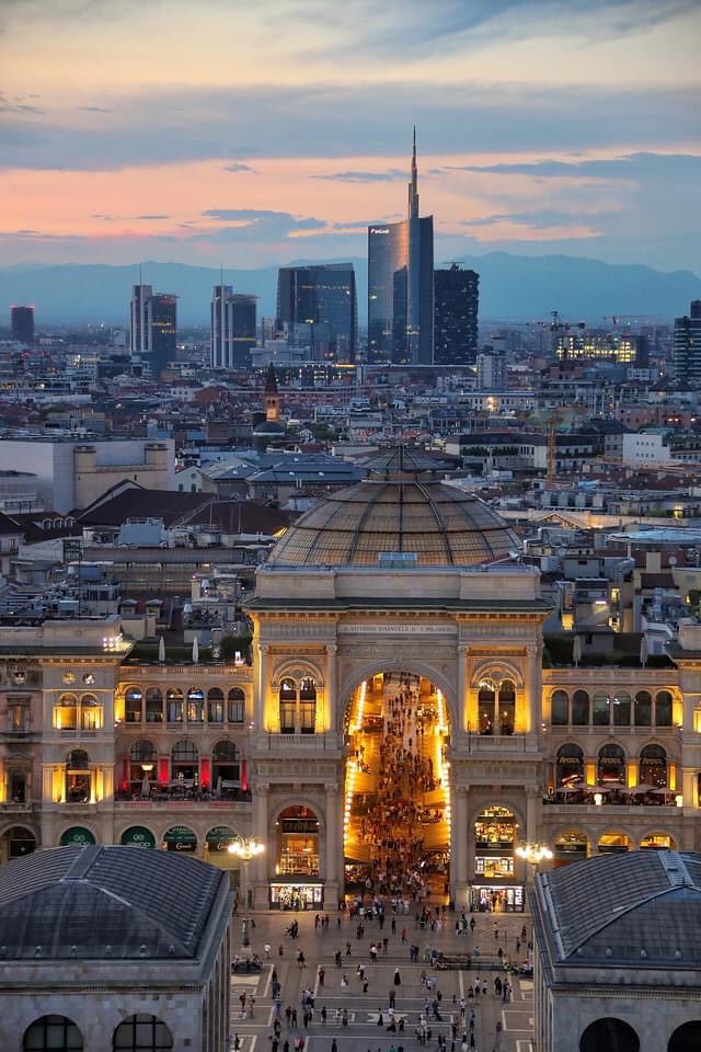 an aerial view of a large building with many lights on it's sides and buildings in the background