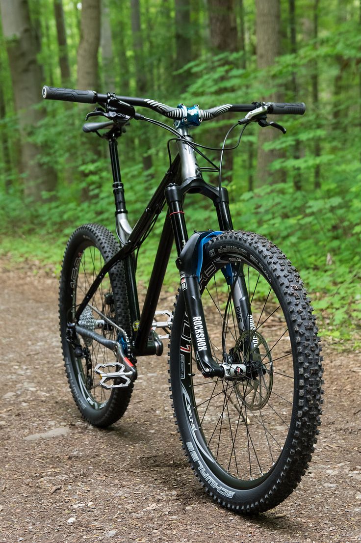 a bicycle parked on the side of a dirt road in front of some trees and bushes