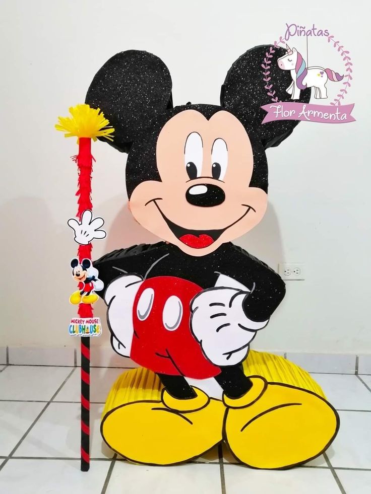 a mickey mouse holding a wand on top of a tile floor in front of a white wall