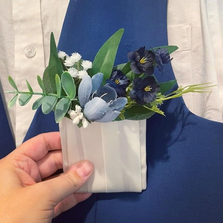 a person is holding a flower arrangement in their lapel coat pocket while wearing a blue suit