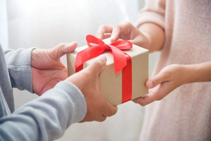 two people holding a gift box with a red ribbon on it and another person's hands