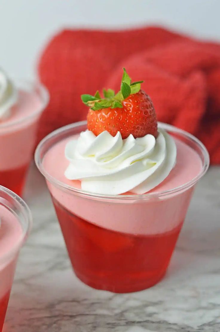 three dessert cups with whipped cream and a strawberry on the top one cup is pink