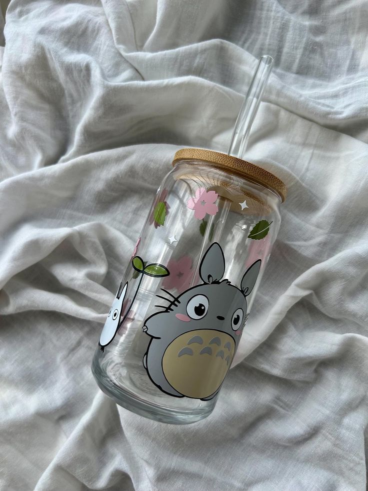 a glass cup with an image of totoro on it sitting on a bed