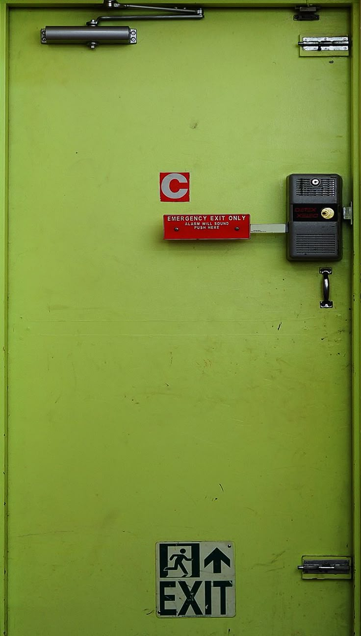 a green door with a red exit sign on the side and a black key attached to it