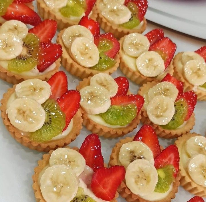 small fruit tarts with kiwis, strawberries and bananas on them are ready to be eaten