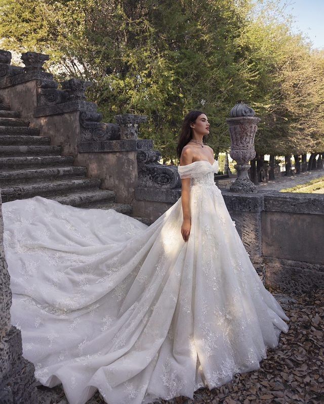 a woman in a white wedding dress standing on some rocks and looking off to the side