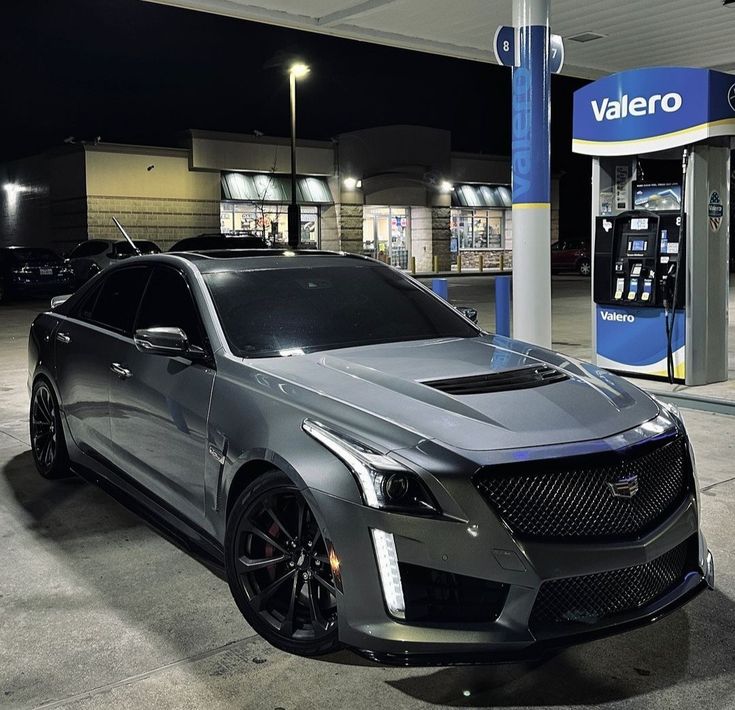 a cadillac parked in front of a gas station at night with its hood up and lights on