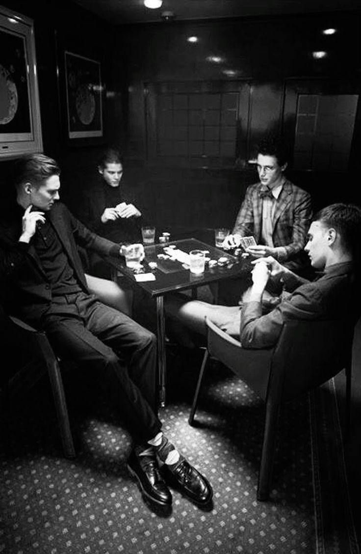 a group of men sitting around a table in a dark room with one man playing cards