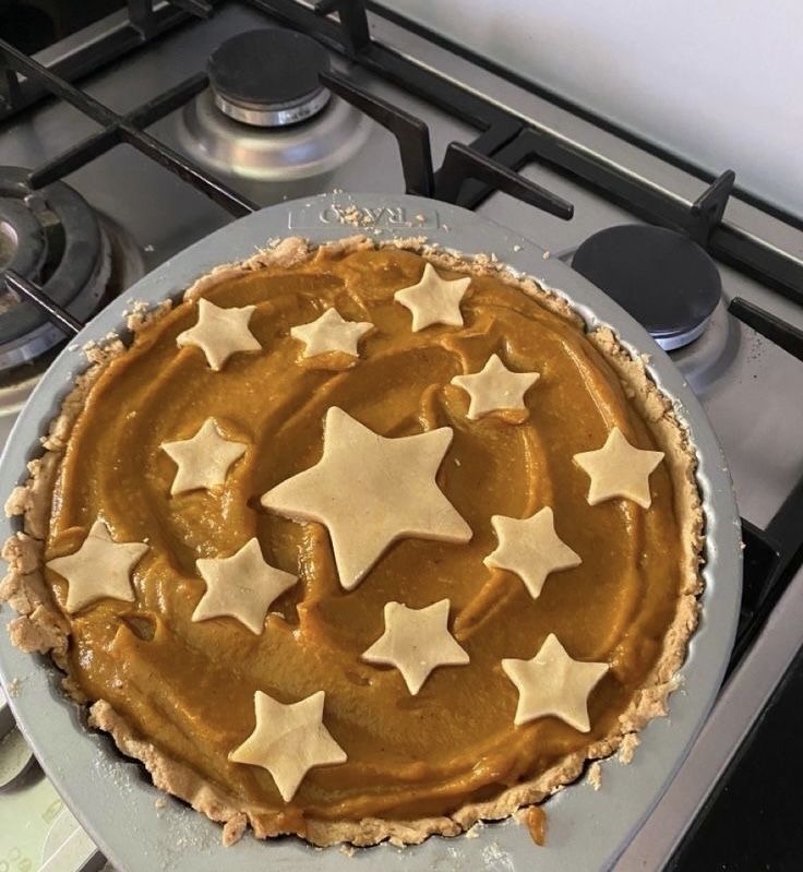 a pie sitting on top of a stove next to a pan filled with stars covered in icing