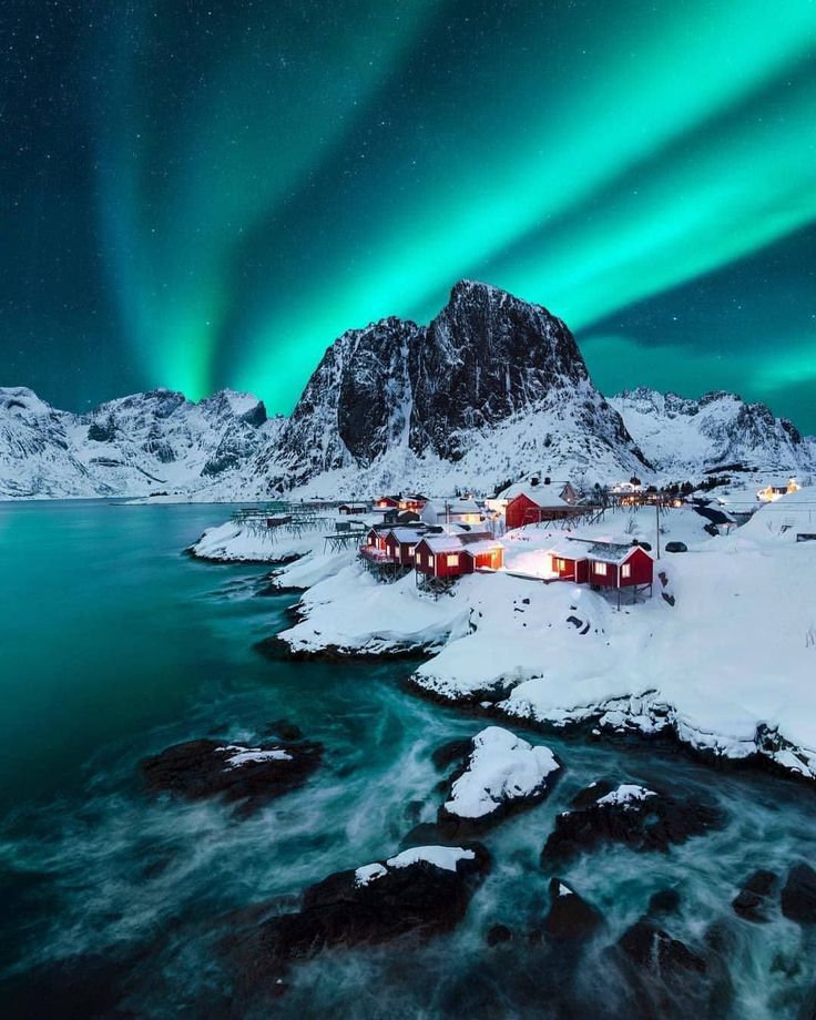 the northern lights shine brightly in the sky above snow covered mountains and small houses on an island