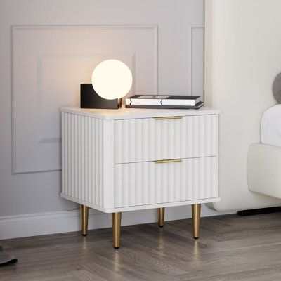 a white nightstand with a lamp on top of it next to a bed and a pair of shoes