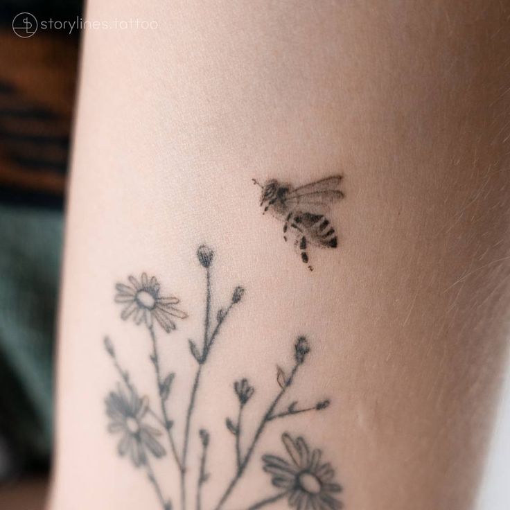 a bee flying over a flower tattoo on the side of a woman's leg