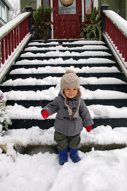 a small child standing on snow covered steps in front of a house with red door