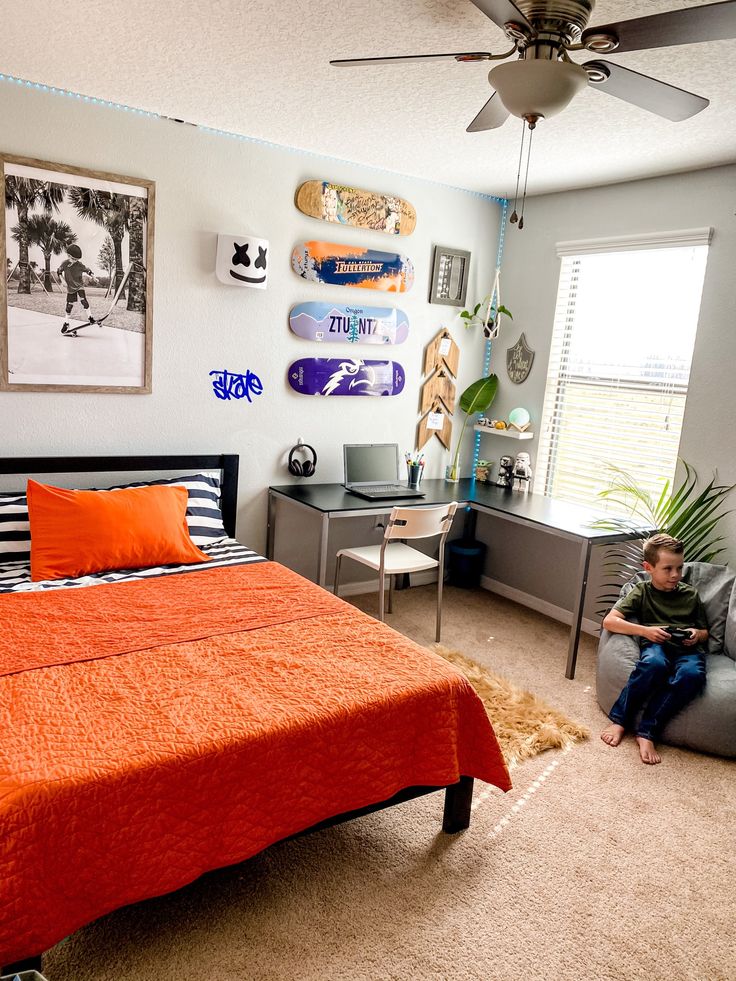 a boy sitting on a chair in front of a bed with an orange comforter