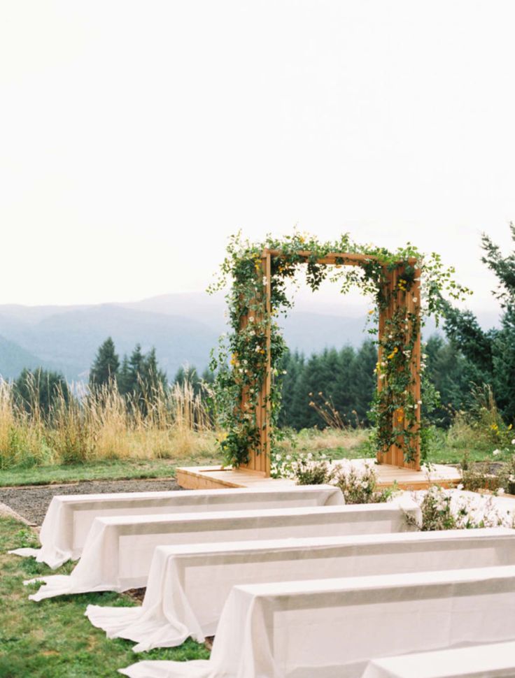 an outdoor ceremony set up with white linens and greenery on the sidelines