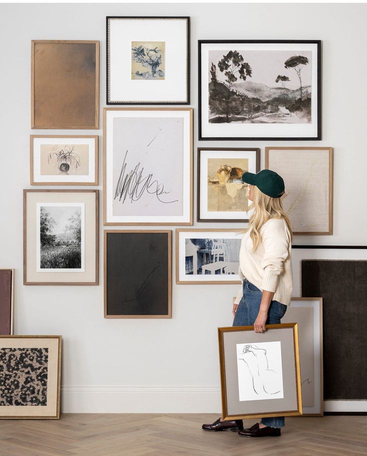 a woman standing in front of a wall filled with pictures and framed art on it