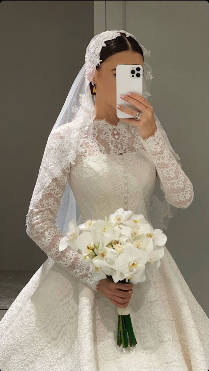 a woman in a wedding dress taking a selfie with her cell phone while holding a bouquet of flowers