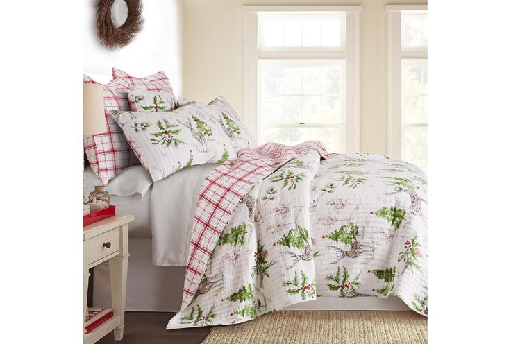 a bed with white and red comforters in front of a window next to a night stand