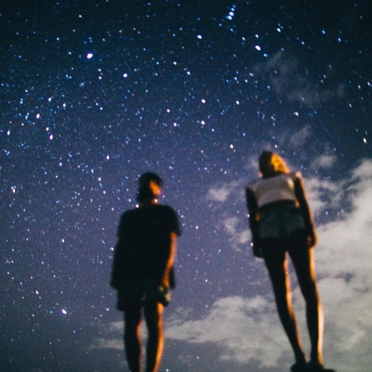 two people looking up at the night sky with stars in the background and clouds below