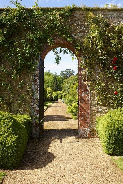 an open gate leading into a lush green garden with flowers and bushes on either side