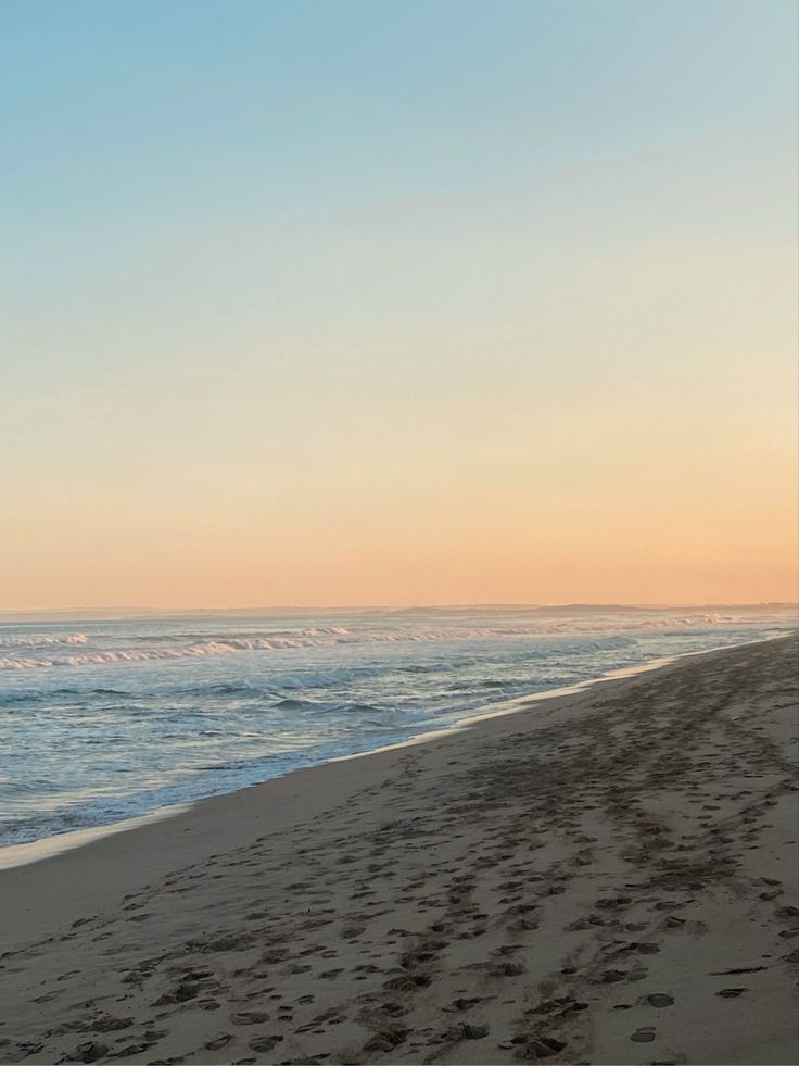 a person walking on the beach with a surfboard in their hand and footprints in the sand