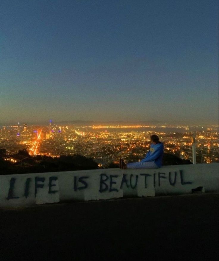 a person sitting on top of a hill with the city lights in the back ground